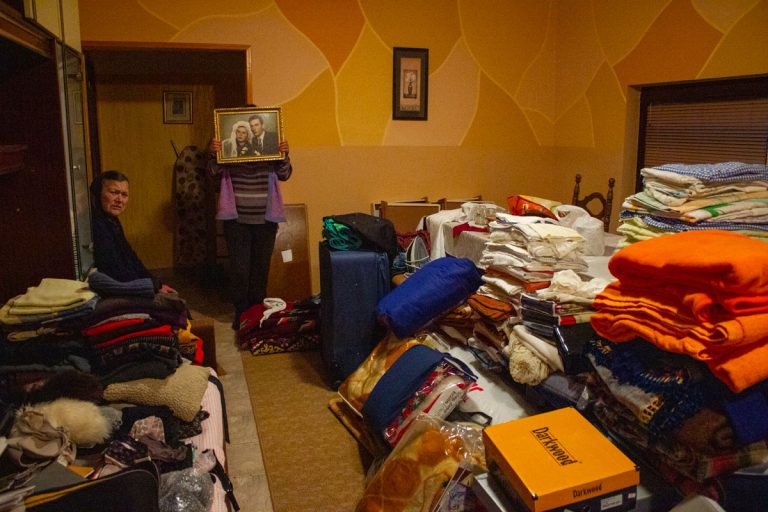 a grandmother and a woman holding an old wedding portrait next to a pile of belongings ready to be sorted