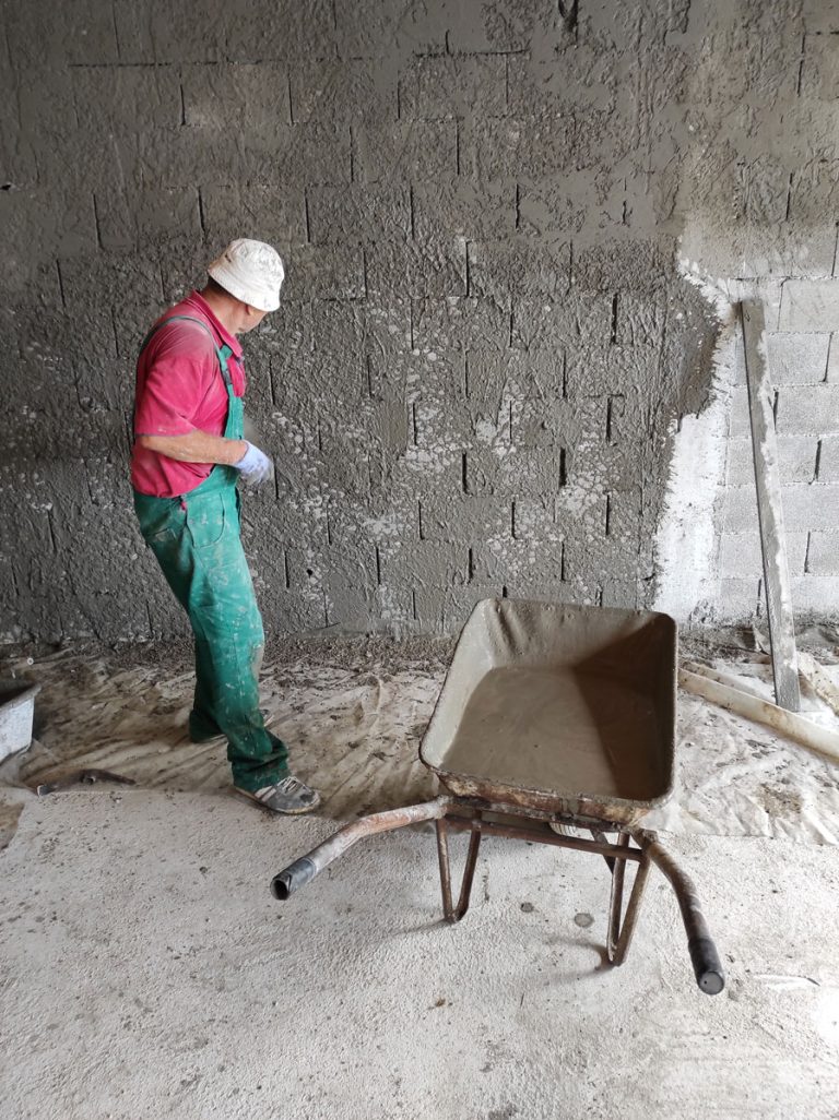 a worker mortaring a wall next to the wheelbarrow