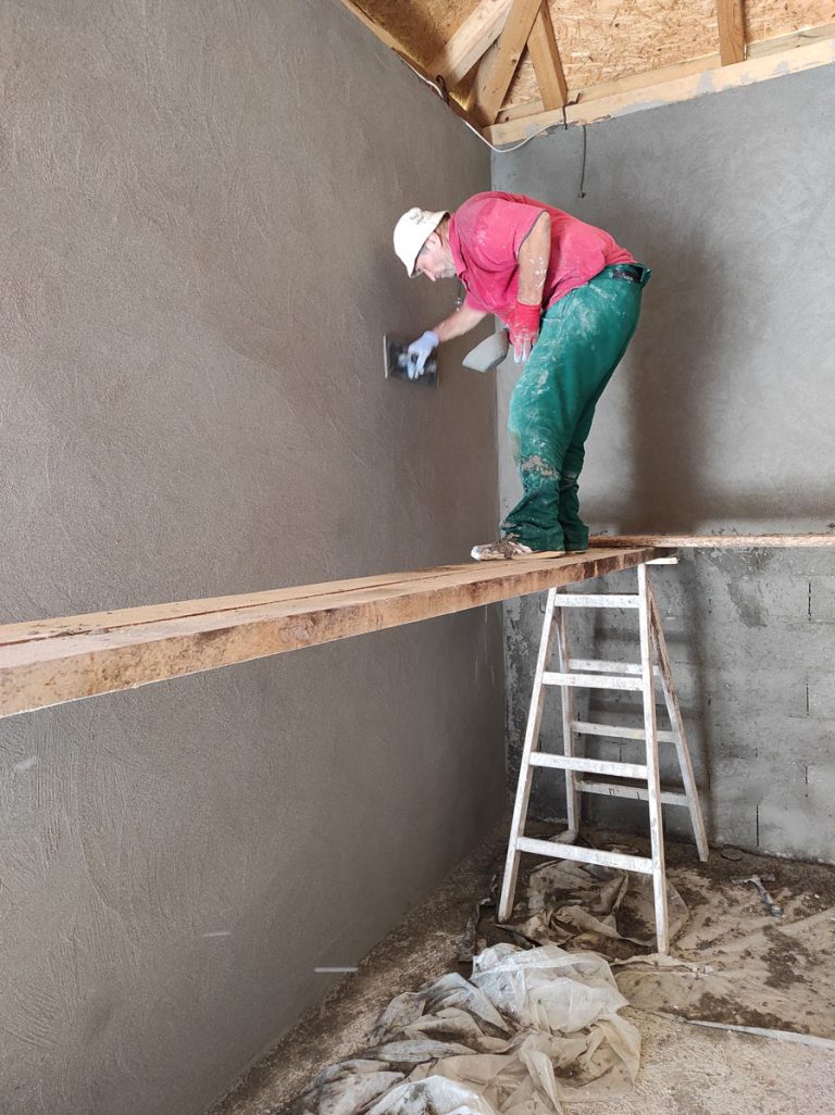 a worker on a scaffolding mortaring a wall in a garage