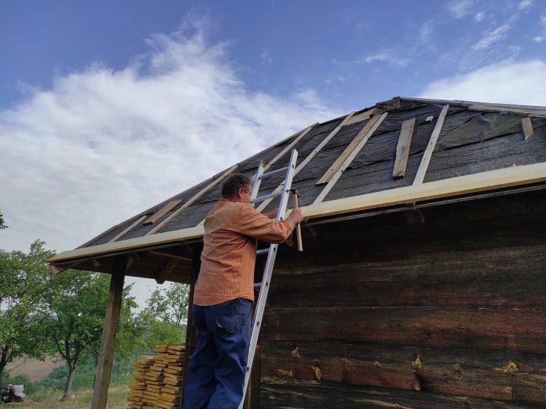 a worker building a new roof on an old wooden cottage