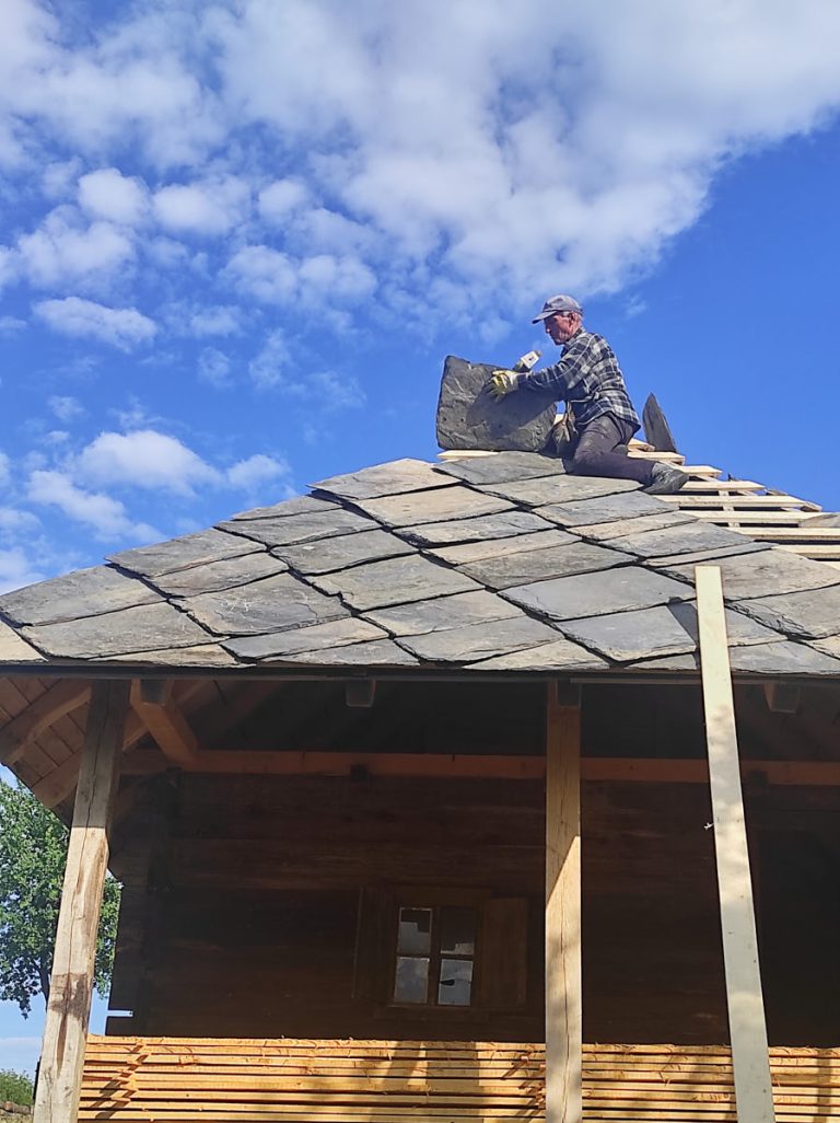 a worker building a new roof on an old wooden cottage