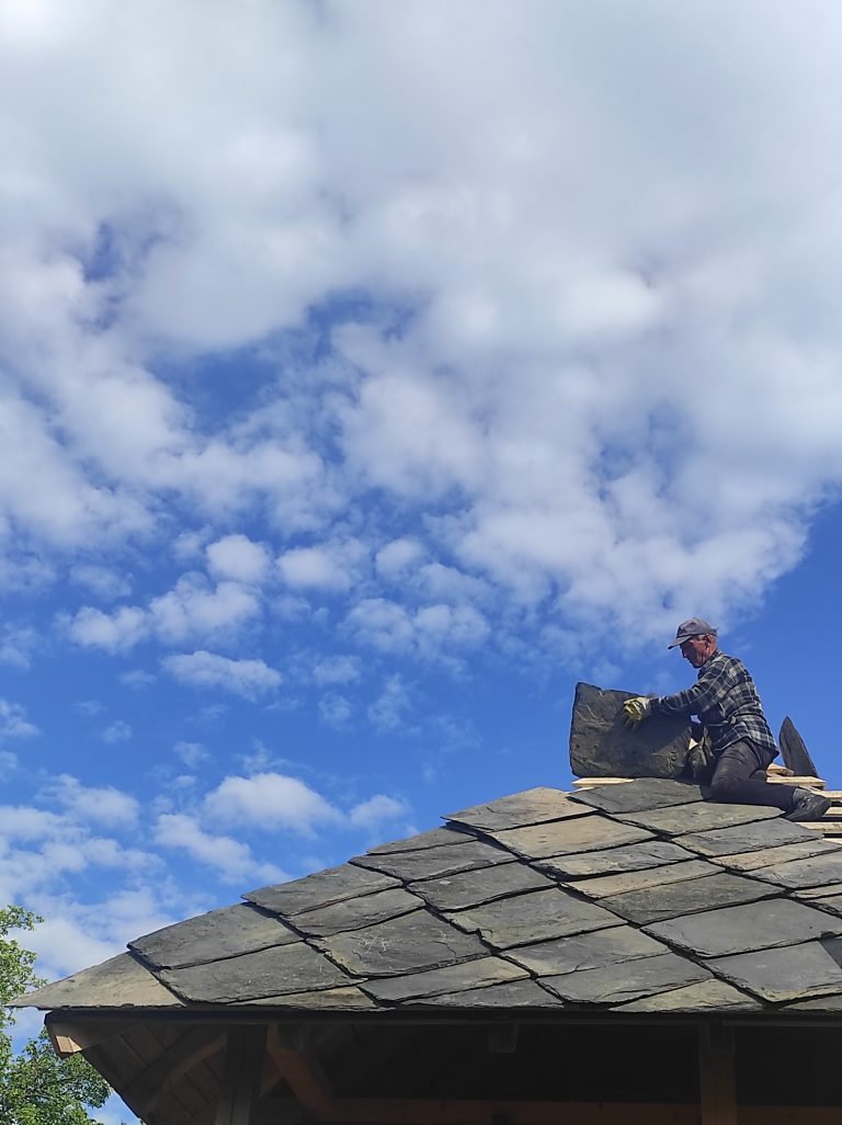 a worker building a new roof on an old wooden cottage