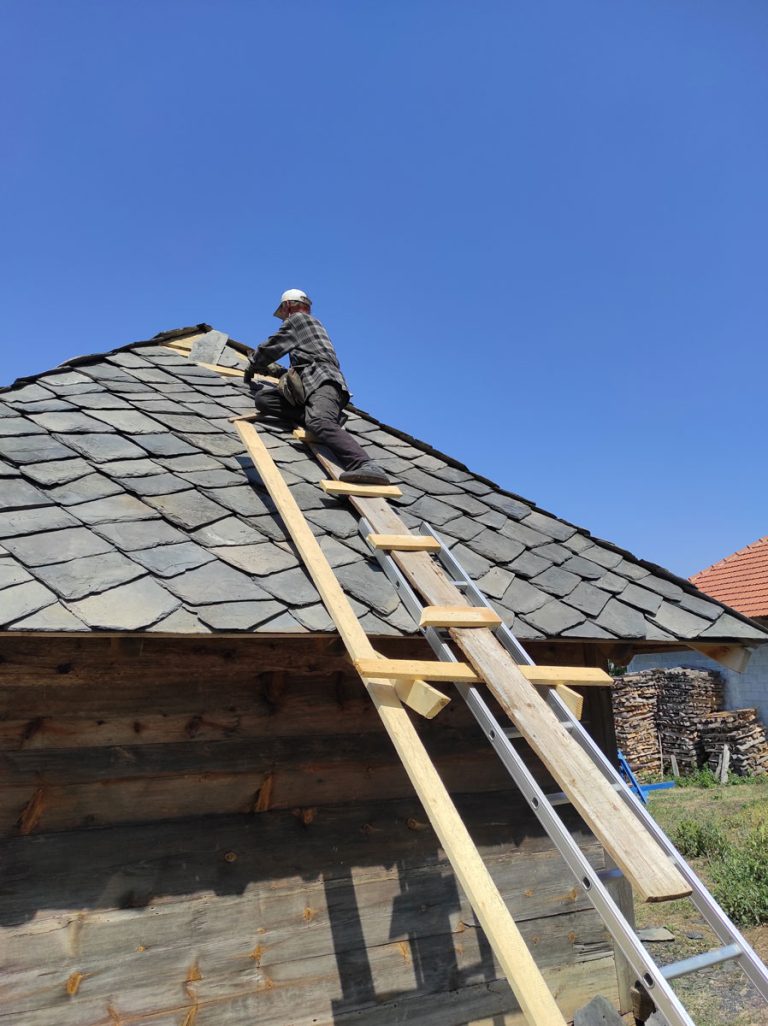 a worker building a new roof on an old wooden cottage