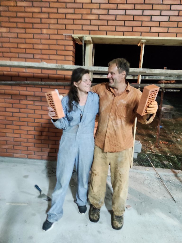 happy workers posing with bricks in their hands by a brick wall