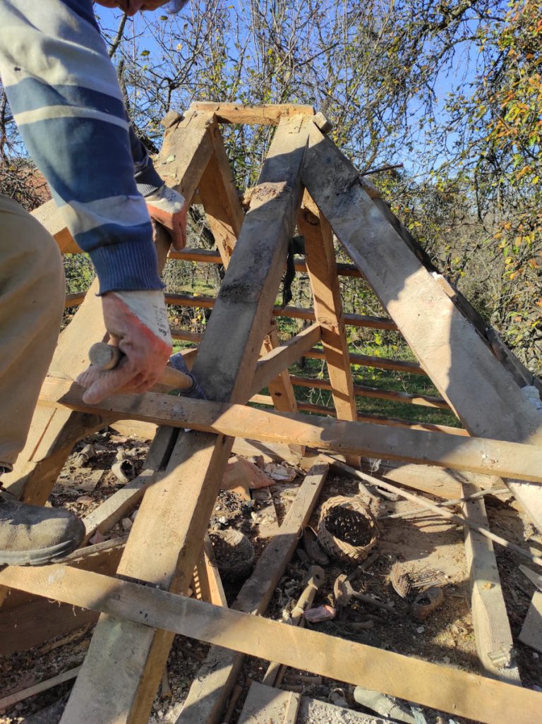 a worker disassembling an old wooden cottage roof construction
