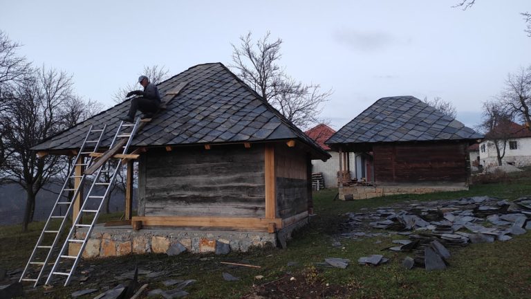 a worker on a wooden cottage roof rebuilding roof tiles