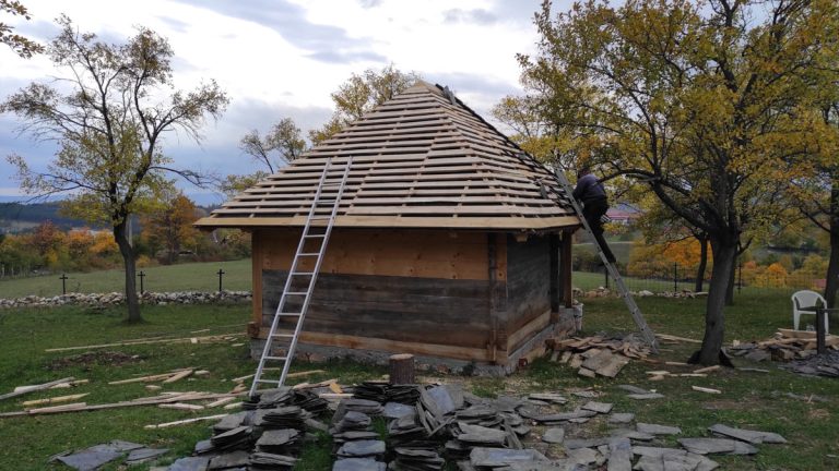 a worker on a wooden cottage roof rebuilding roof tiles