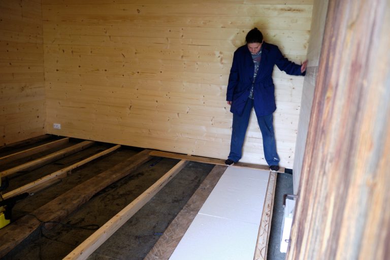 a woman in a wooden cottage installing styrofoam isolation