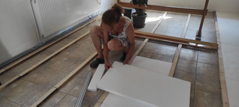 a woman installing styrofoam boards between floor planks