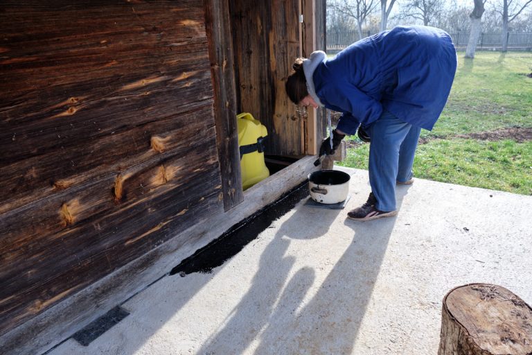 a woman placing bitumen on a cottage porch